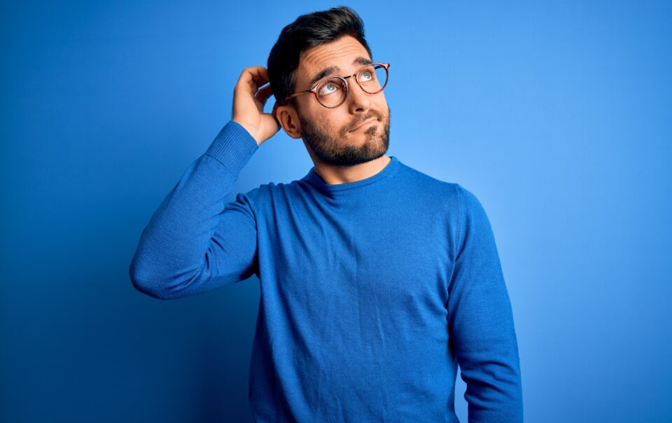 young handsome man with beard wearing casual sweater glasses blue background confuse wondering about question uncertain with doubt thinking with hand head pensive concept