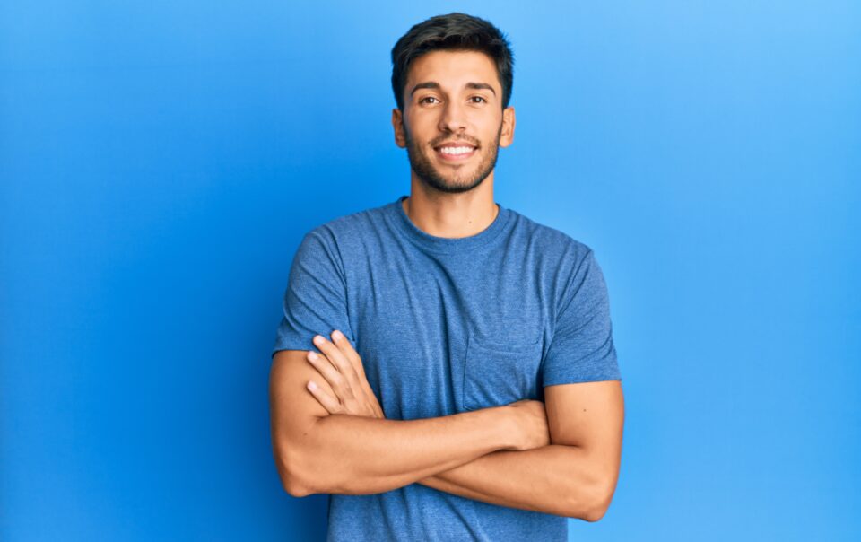 young handsome man wearing casual tshirt blue background happy face smiling with crossed arms looking camera positive person